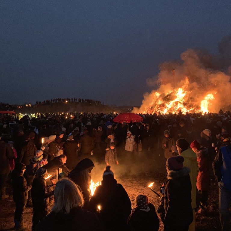 Nachts versammelt sich eine große Menschenmenge um ein Lagerfeuer.