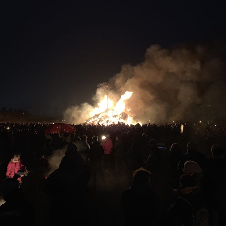 Nachts versammelt sich eine große Menschenmenge um ein Lagerfeuer.