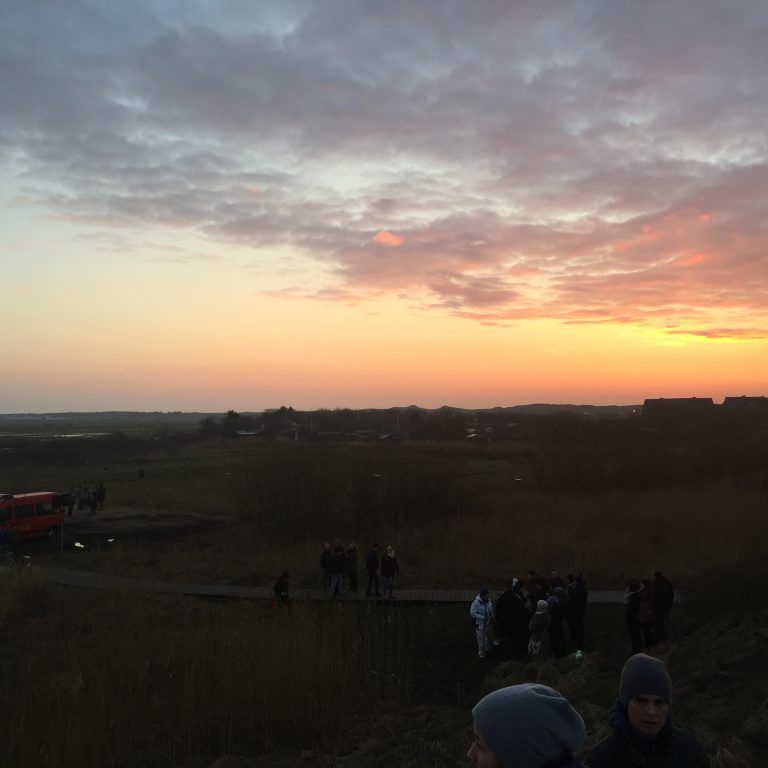 Eine Gruppe von Menschen steht bei Sonnenuntergang auf einem Feld.